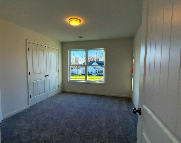 Empty bedroom with carpeted flooring, built-in closet doors, and large window with natural light