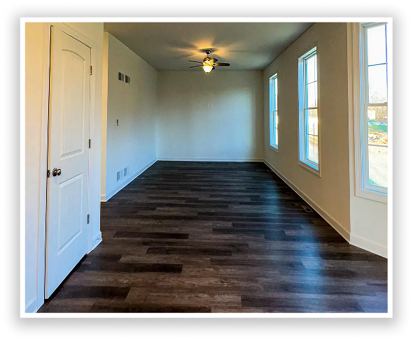 Empty living room with dark wood flooring, ceiling fan, and large windows bringing in natural light